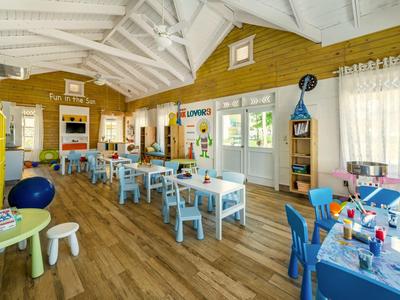 Sala de juegos luminosa y acogedora con suelo de madera y mesas pequeñas para niños.