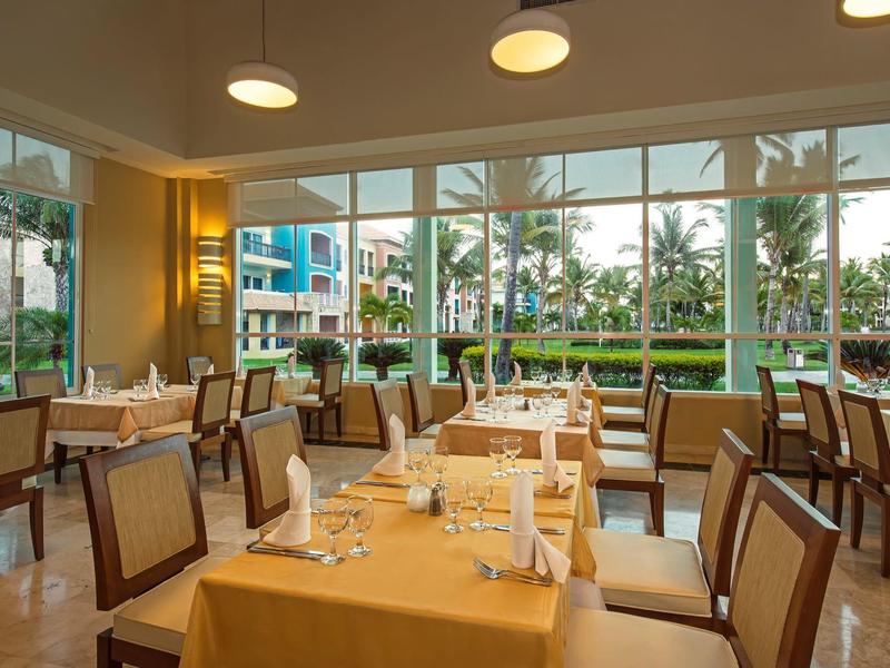 Restaurante luminoso con grandes ventanales con vista a palmeras y área exterior.