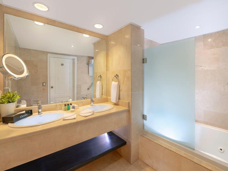 Baño luminoso con lavabo doble y bañera detrás de una pared de vidrio.