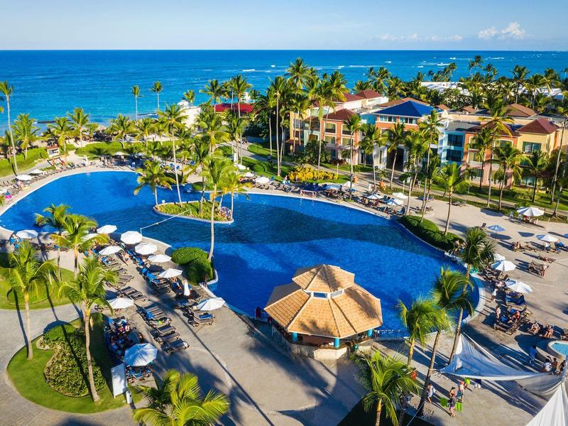 Gran piscina del resort con tumbonas y palmeras junto al mar.