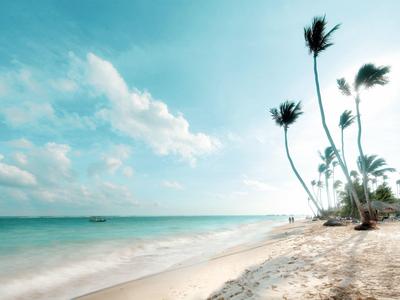 Strand mit weißem Sand, türkisfarbenem Wasser und hohen Palmen unter blauem Himmel mit Wolken.