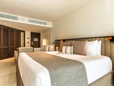 Chambre d'hôtel lumineuse avec grand lit double, meubles en bois et climatisation murale.