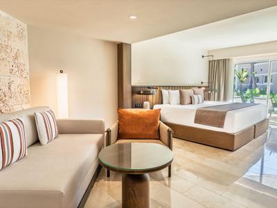 Camera d'hotel luminosa con letto grande, divano, poltrona e terrazza con vista sul giardino.