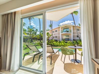 Vista da una stanza attraverso una porta scorrevole in vetro su una terrazza con tavolo, sedie e giardino.