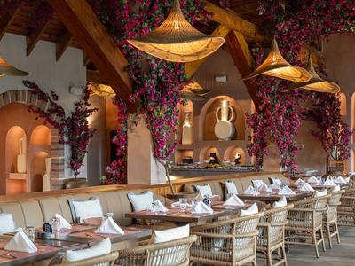 Ristorante elegante con soffitto a travi di legno, lampade sospese e interni decorati con fiori.