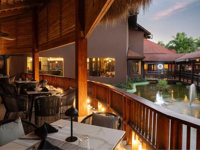 Accogliente terrazza ristorante all'aperto con vista su uno stagno e edificio di hotel di lusso al crepuscolo.