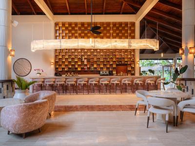 Ristorante moderno in hotel con soffitto in legno, sgabelli lunghi e poltrone di velluto.