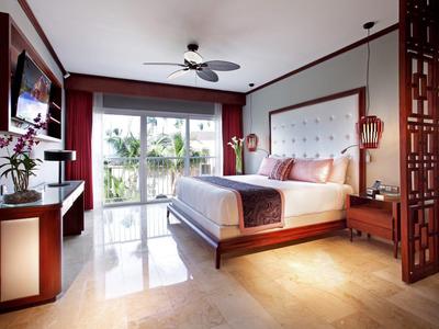 Modernes Hotelzimmer mit großem Bett, Deckenventilator und Balkon mit Blick auf Palmen.