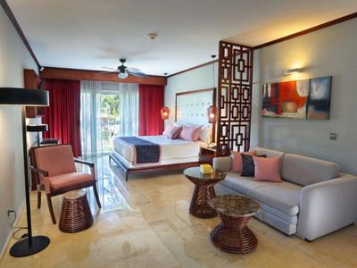 Helles Hotelzimmer mit Doppelbett, Sofa, Sesseln und Balkon mit Gartenblick.