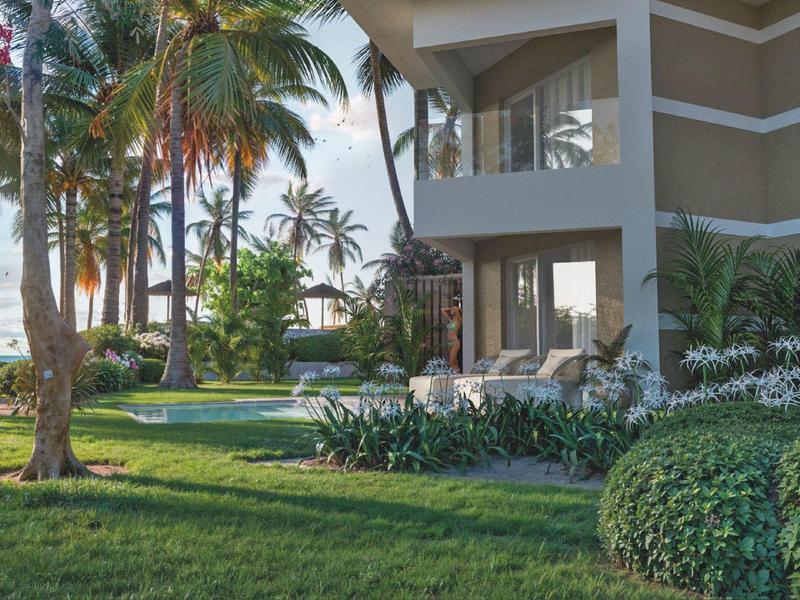 Moderní hotelový balkon s výhledem na zelenou zahradu a bazén za slunečného dne.