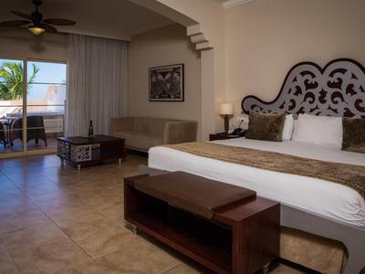 Spacious hotel room with king-size bed, seating area, and balcony with sea view.