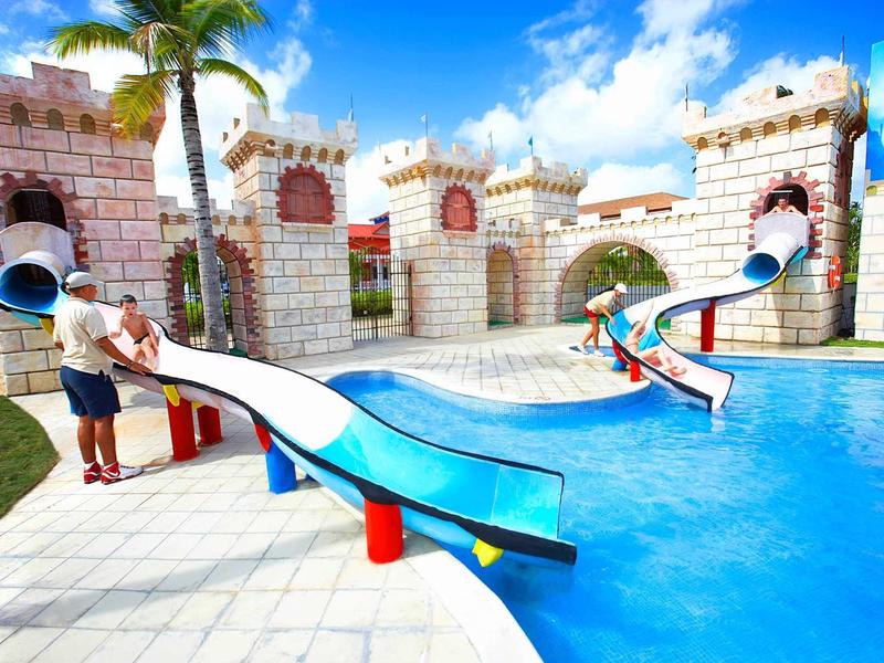 Children playing on slides leading into a pool in a castle-themed water park.
