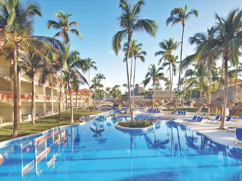 Large pool with palm trees and lounge chairs in a sunny hotel resort.