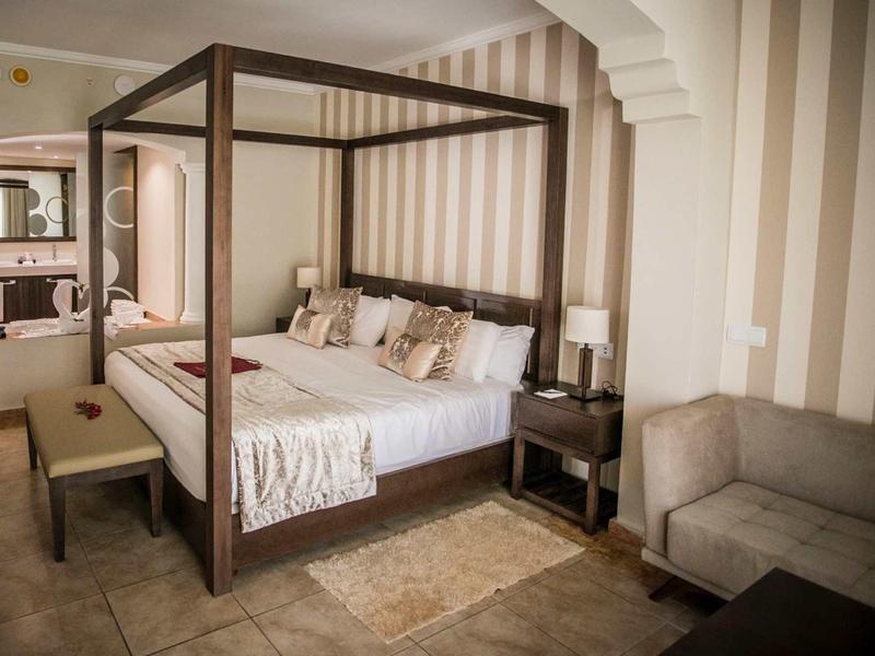 Elegant hotel room with canopy bed, seating area, and striped walls.