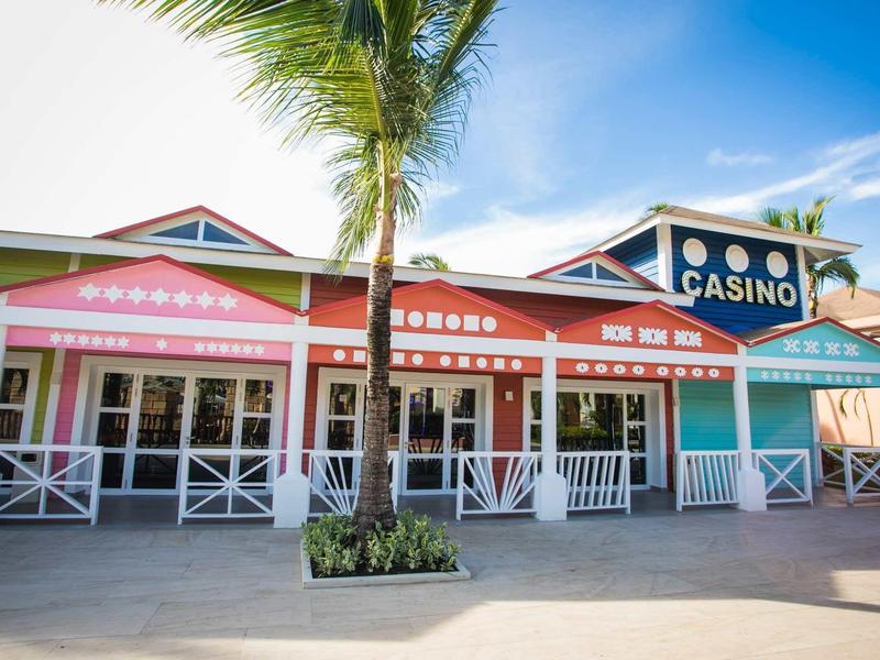 Colorful casino and shop facades under a blue sky with palm trees.