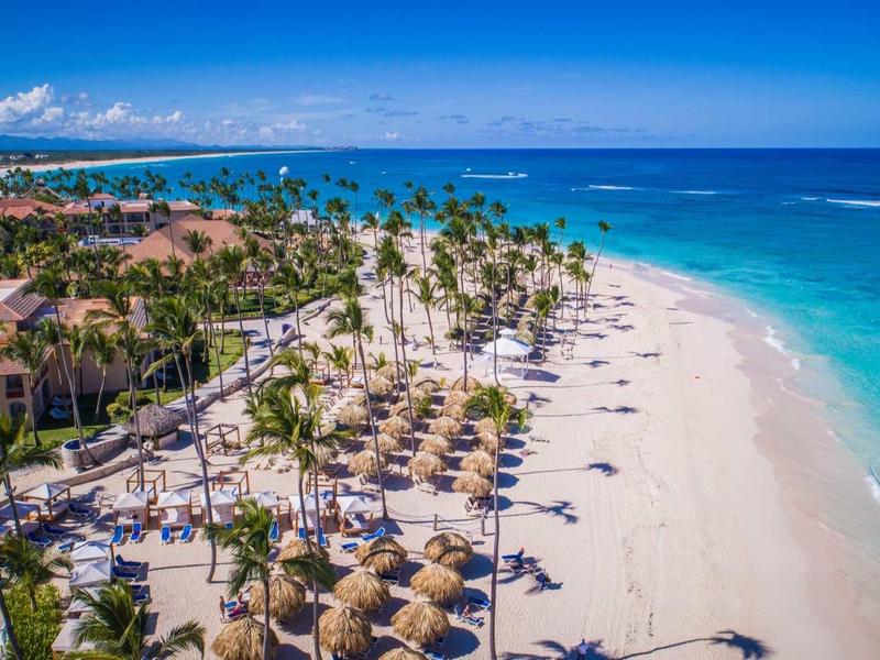 Aerial view of a tropical beach with palm trees, sand, and resort areas.