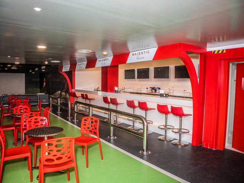 Modern bar with red chairs and stools, green floor, and white ceiling.