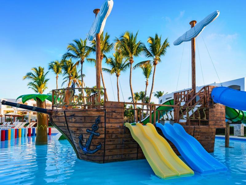 Parc aquatique avec structure pirate et toboggans pour enfants dans une piscine sous un ciel bleu.