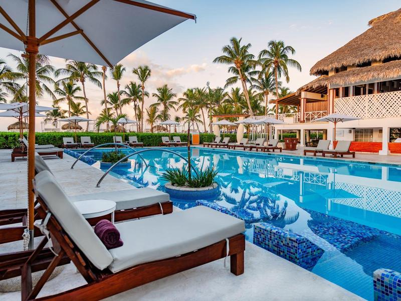 Espace piscine luxueux avec chaises longues, parasols et palmiers dans un complexe hôtelier.