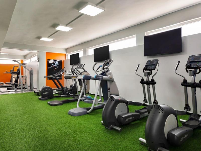 Salle de sport moderne avec tapis roulants et appareils elliptiques sur sol vert.