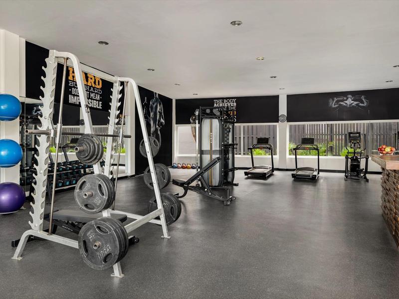 Salle de sport moderne avec équipements, haltères et tapis de course dans une pièce lumineuse.