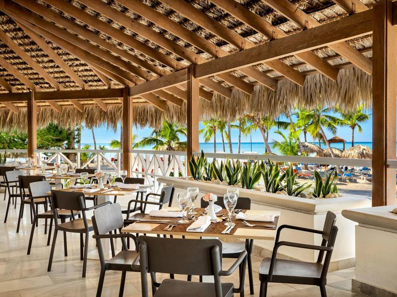 Terrasse de restaurant de plage avec vue sur des palmiers et la mer.