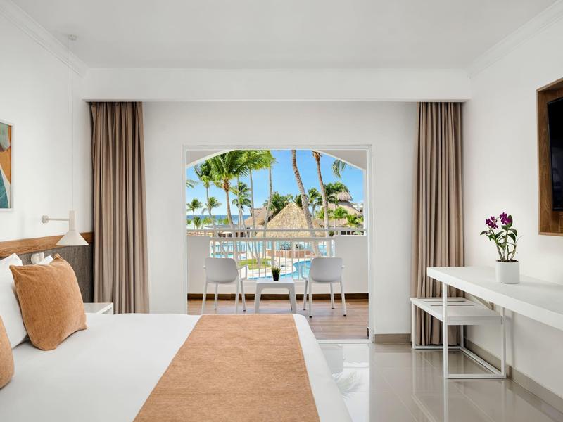Chambre d'hôtel moderne avec lit double, bureau et balcon avec vue sur les palmiers.