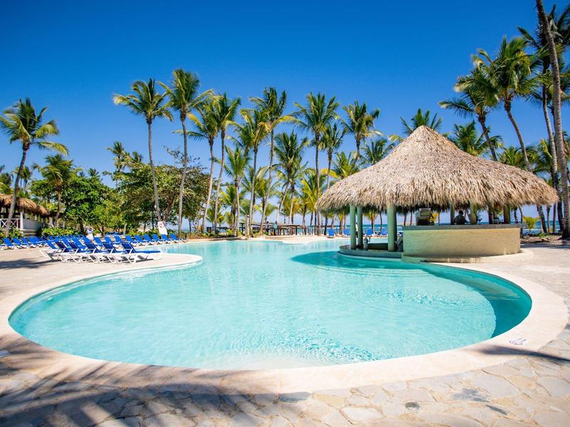 Round pool with thatched roof bar and palm trees under clear sky.