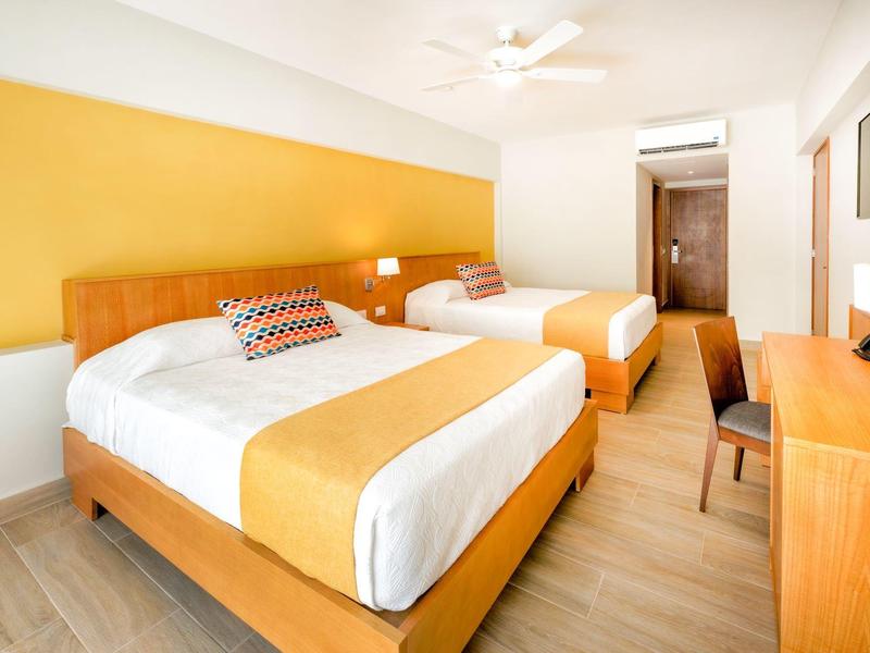 Hotel room with two beds, wooden furniture, and yellow accent wall.