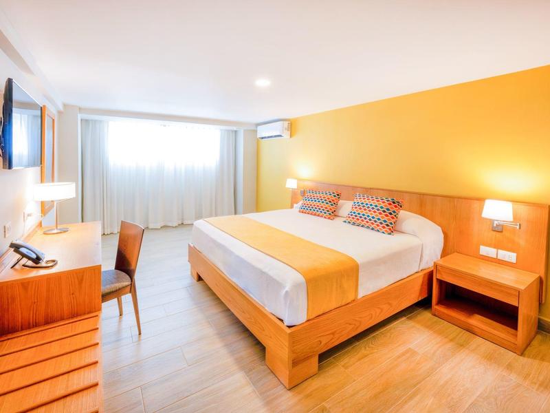 Bright hotel room with double bed, wooden furniture, and yellow accent wall.