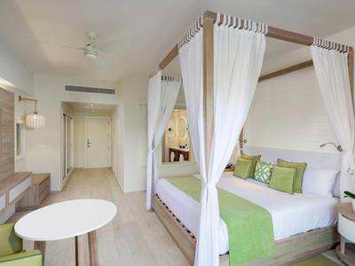 Helles Hotelzimmer mit Himmelbett, weiß-grüner Dekoration und modernem Mobiliar.