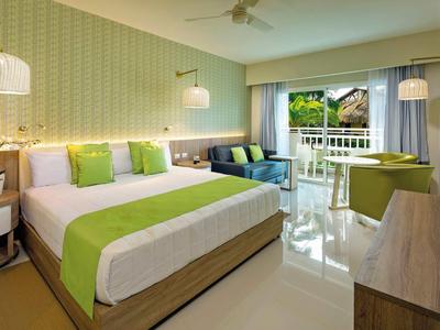 Modern eingerichtetes Hotelzimmer mit großem Bett und Balkon mit Blick auf tropische Pflanzen.