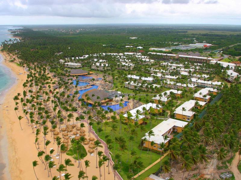 Luftaufnahme eines tropischen Strandes mit Palmen, blauen Pools und weißen Gebäuden am Meer.