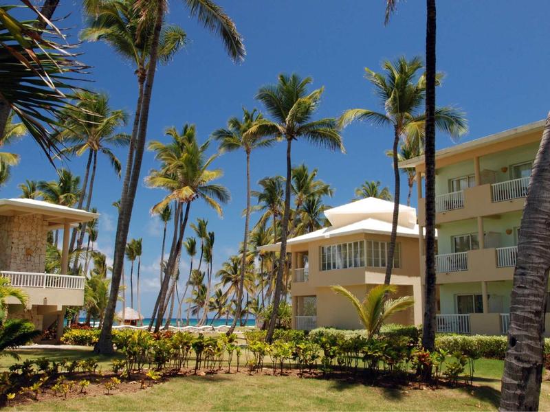 Blick auf tropische Hotelanlage mit Palmen, grünen Pflanzen und strahlend blauem Himmel.