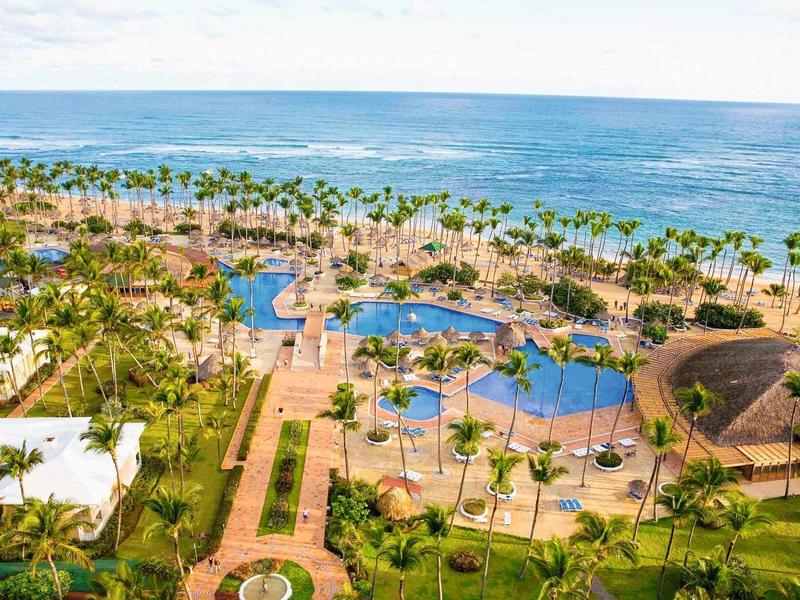 Strandresort mit Palmen, Pools, Wegen und weiter Sicht auf das blaue Meer und den Himmel.