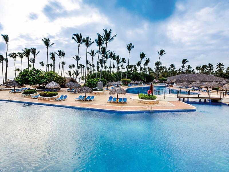 Großer blauer Pool mit Insel und Palmen bei bewölktem Himmel in tropischem Resort.
