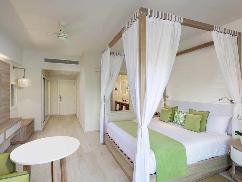 Helles Hotelzimmer mit Himmelbett, weiß-grüner Dekoration und modernem Mobiliar.