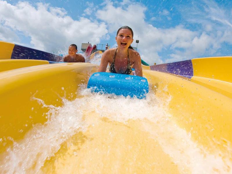 Frau fährt auf blauem Reifen eine gelbe Wasserrutsche bei sonnigem Himmel hinab.