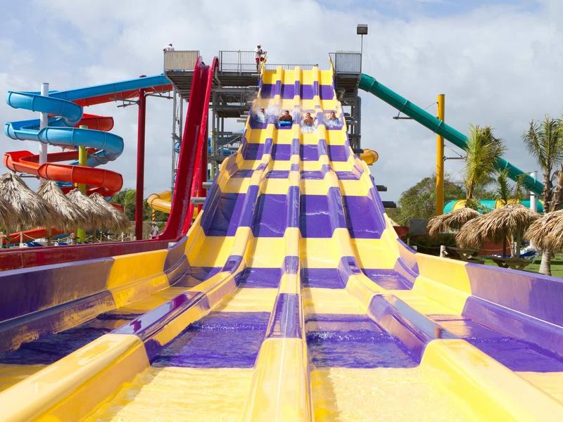 Mehrspurige Wasserrutsche in Gelb und Lila mit bunten Röhrenrutschen im Hintergrund.