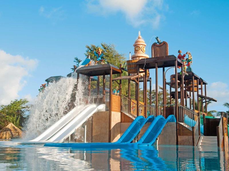 Wasserpark mit Wasserrutschen, Wasserspielen und bunten Bauwerken unter blauem Himmel.