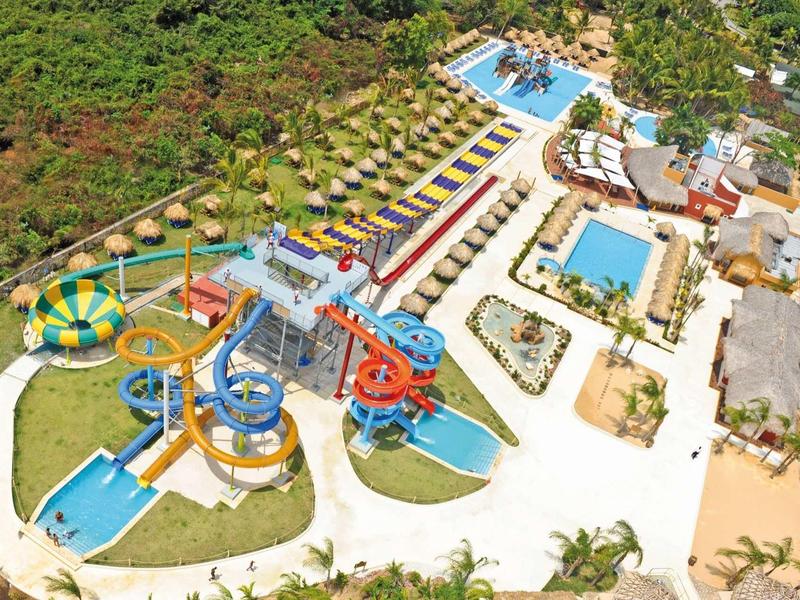 Großer Wasserpark mit bunten Rutschen, Pools, Liegestühlen und viel Grün rundherum.