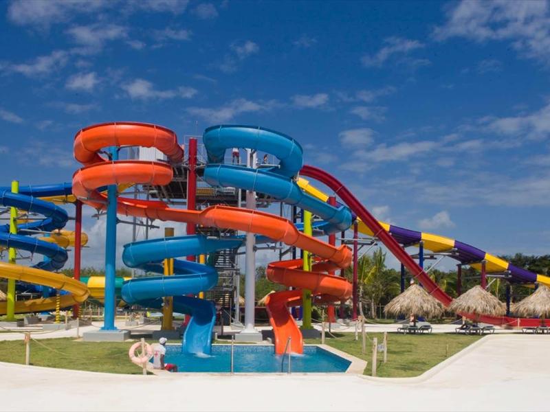 Wasserpark mit bunten Rutschen in Blau, Rot und Gelb vor blauem Himmel und grünem Rasen.