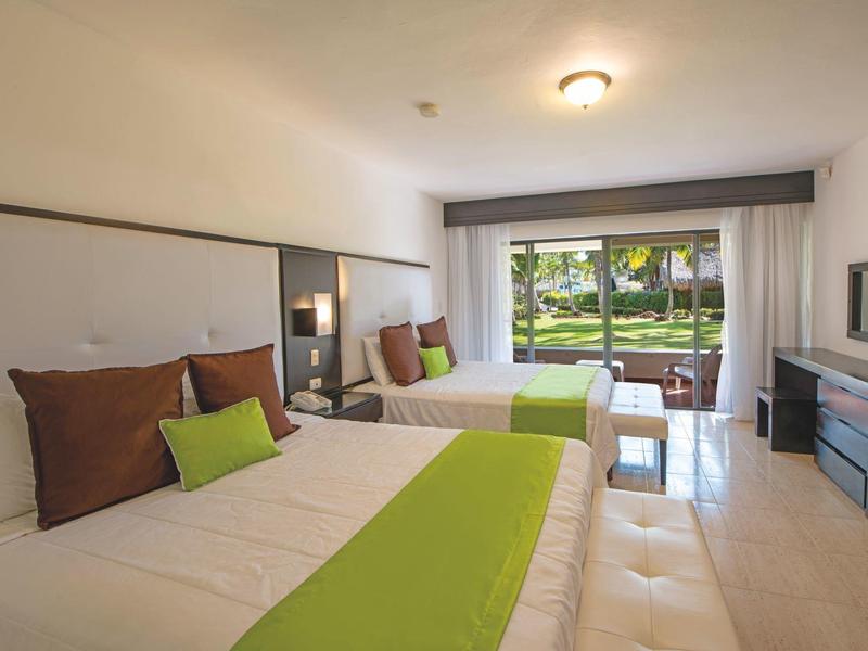 Bright hotel room with two double beds and a view of a garden.