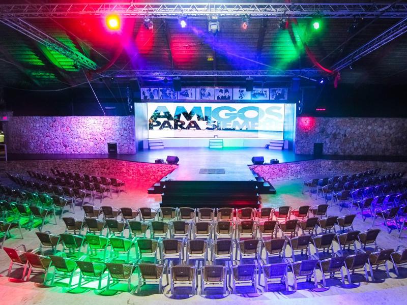 Large event hall with stage and rows of chairs under colorful lights