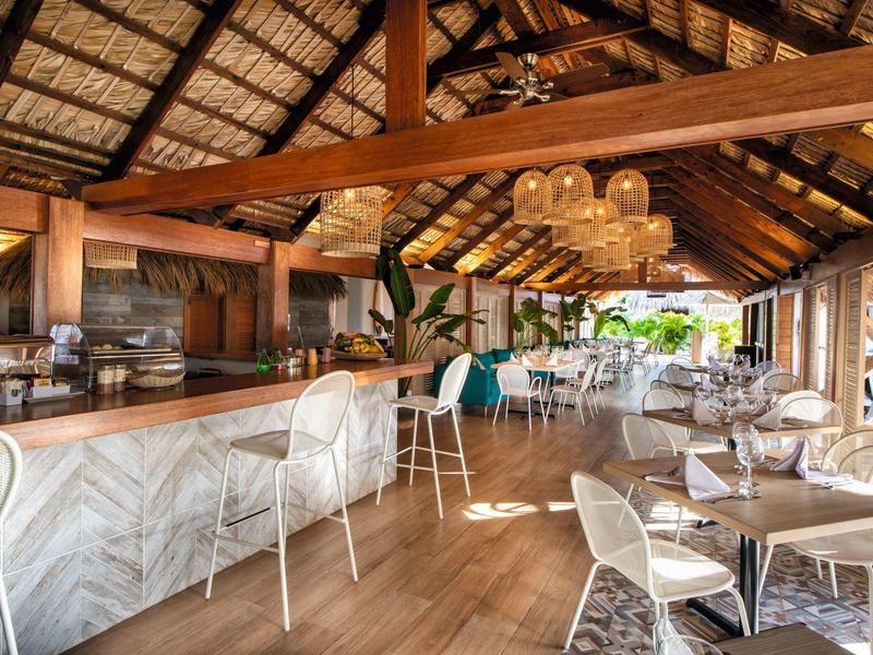 Modern beach restaurant with bamboo roof, white chairs, and wooden floor