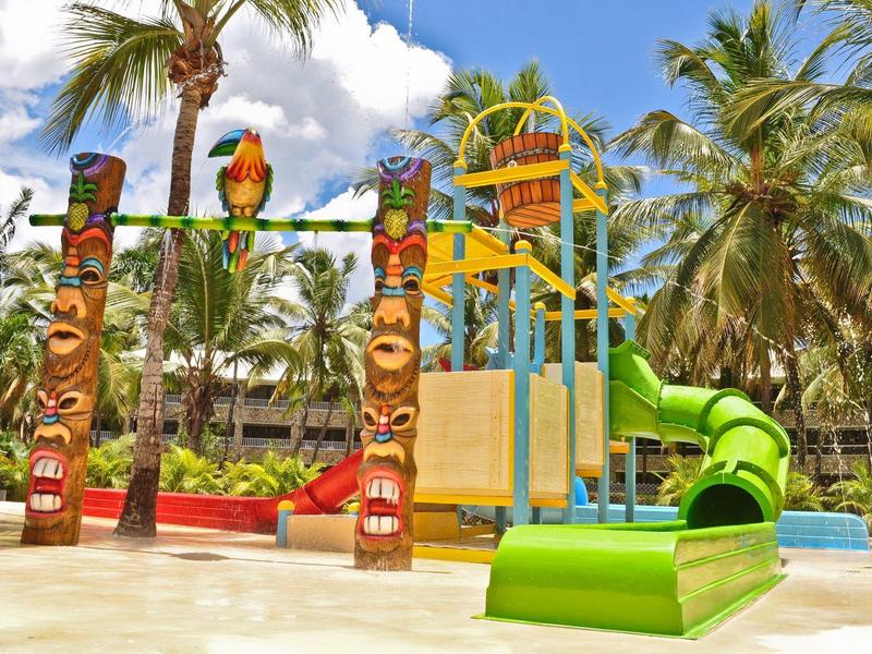 Colorful children's playground with slide and totem poles surrounded by palm trees at a resort
