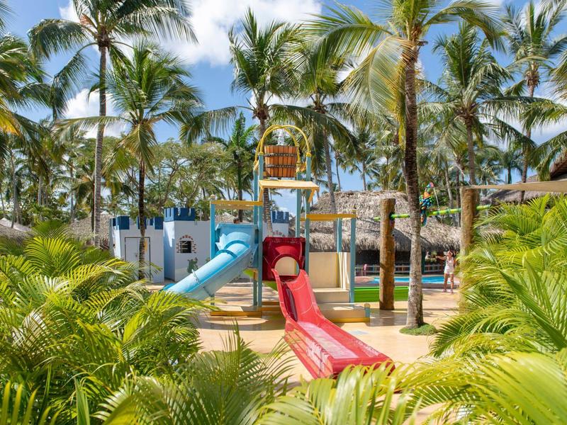 Colorful children's playground with slides surrounded by palm trees in a tropical hotel resort.