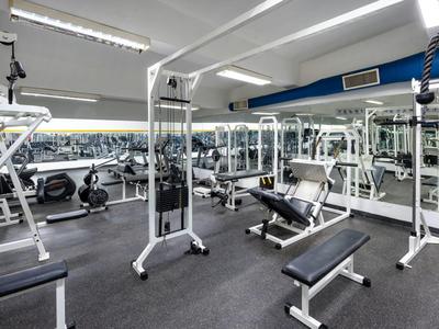 Heller Fitnessraum mit Spiegelwänden, verschiedenen Trainingsgeräten und grauem Teppichboden.
