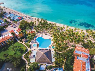 Luftaufnahme eines Resorts mit Pool, Palmen, Sandstrand und türkisfarbenem Meer am Ufer.