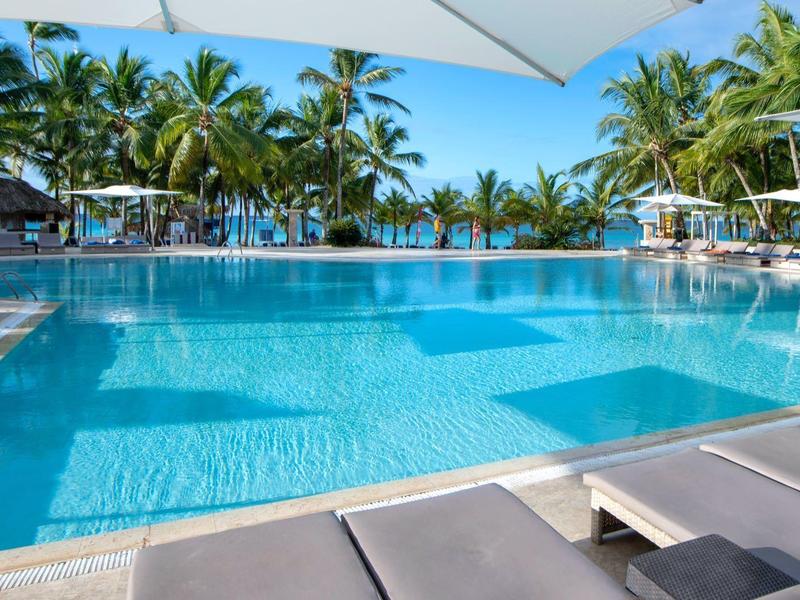 Grand piscine avec palmiers et transats dans une station tropicale par une journée ensoleillée.